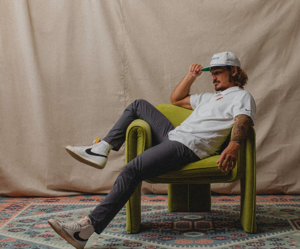 A person in casual attire lounges comfortably on a vibrant green chair, set against a beige backdrop with patterned flooring.
