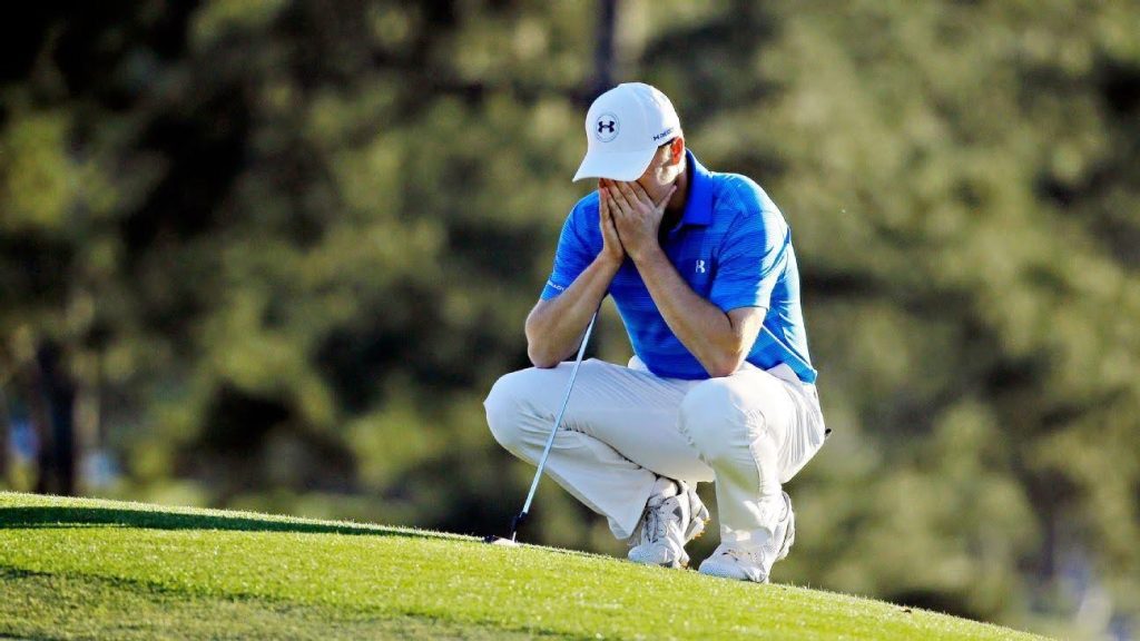 Frustrated golfer crouching on green with head in hands, holding a putter.