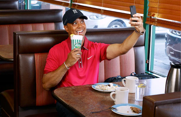 Tiger Woods taking selfie in diner booth while holding Perkins cup.