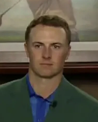 Jordan Spieth wearing green jacket and blue shirt, looking serious indoors.