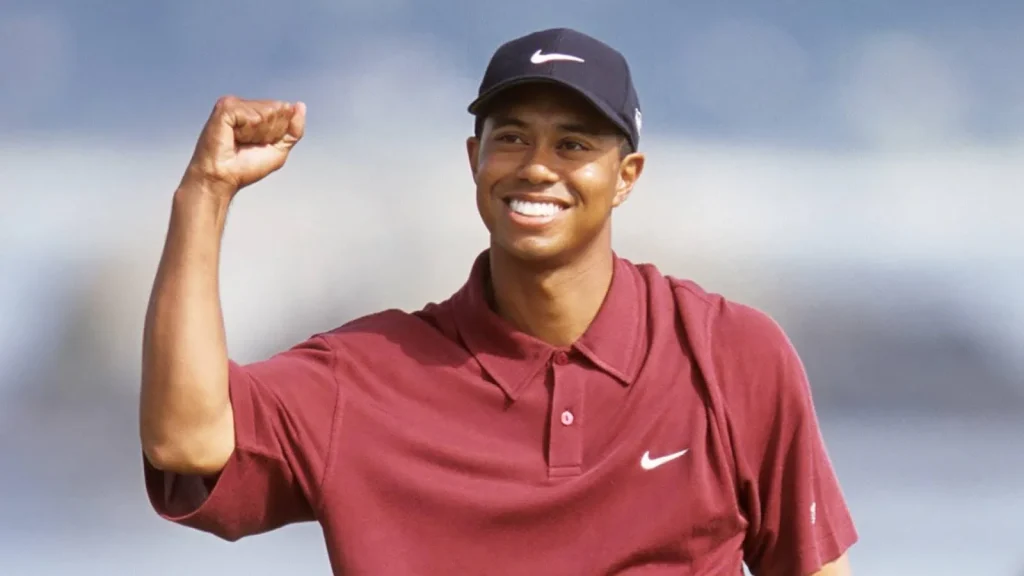 Tiger Woods smiling and raising his fist in a red Nike shirt and cap.